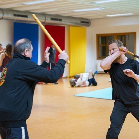 Zwei Männer mit Escrima-Stöcken üben Kampfsporttechniken miteinander