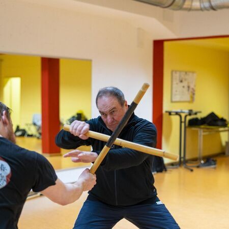 Zwei Männer mit Escrima-Stöcken üben Kampfsporttechniken miteinander